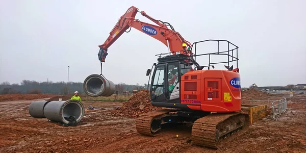 Two Clumber excavators and a crane lowering concrete into a trenchbox